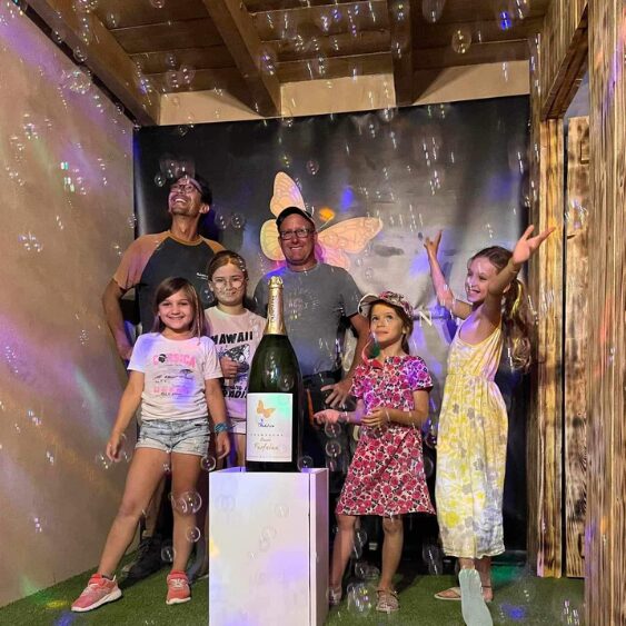 Cinq personnes posant joyeusement avec des bulles et une grande bouteille sur un socle.