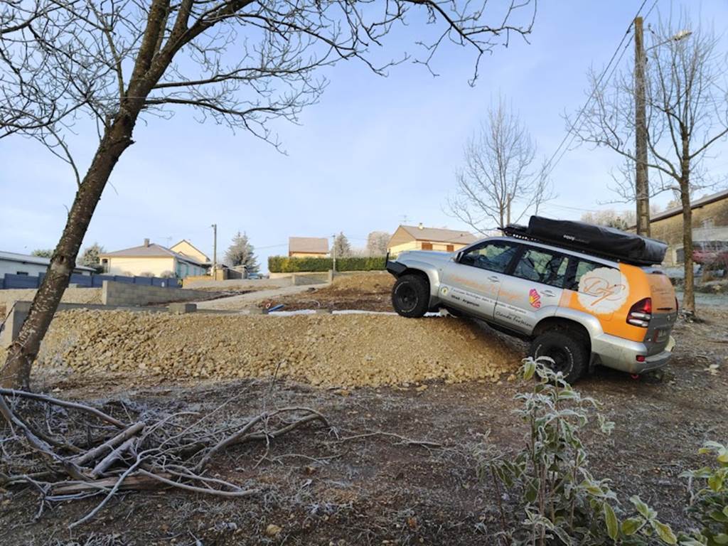 SUV partiellement sur un tas de gravier dans une zone résidentielle avec arbres dénudés.
